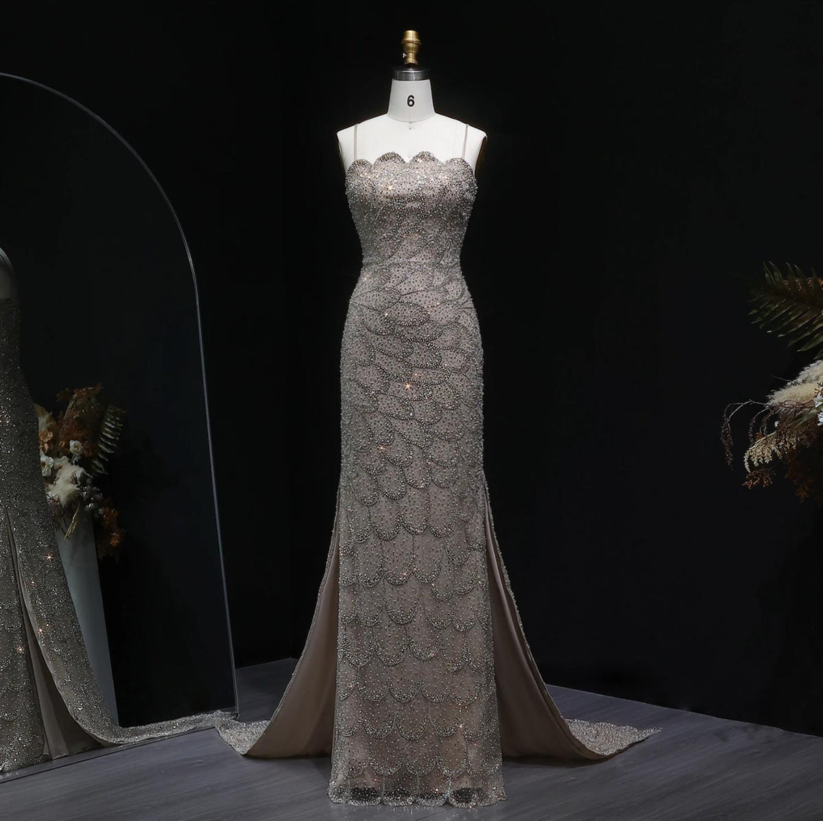 Strapless emerald green mermaid gown with intricate crystal beading, tulle overlay, and a sweeping train on a mannequin.