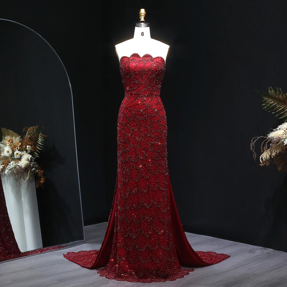 Strapless red mermaid gown with intricate crystal beading, scalloped neckline, and sweeping train on a mannequin.