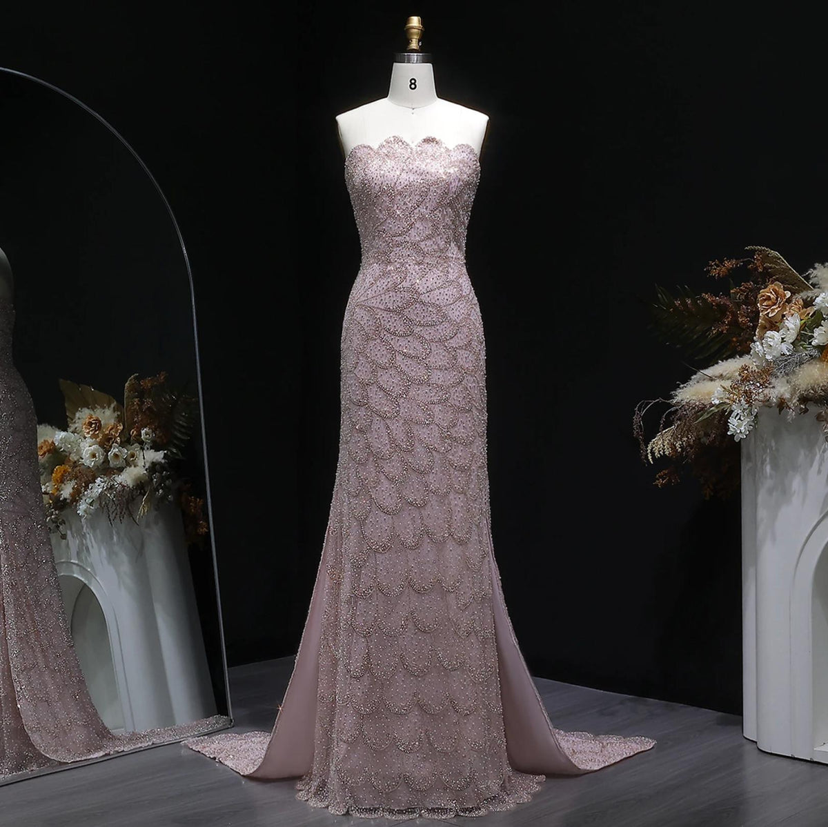 Strapless blush pink mermaid gown featuring intricate crystal beading, tulle fabric, and a sweeping train on a mannequin.