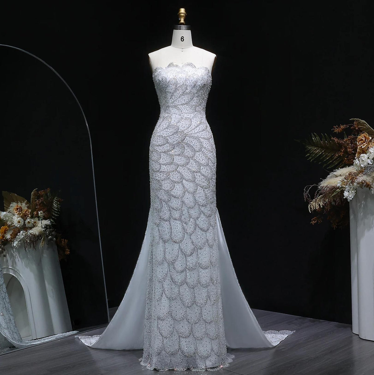 Strapless white mermaid gown with intricate crystal beading, scalloped patterns, and a sweeping tulle train on a mannequin.