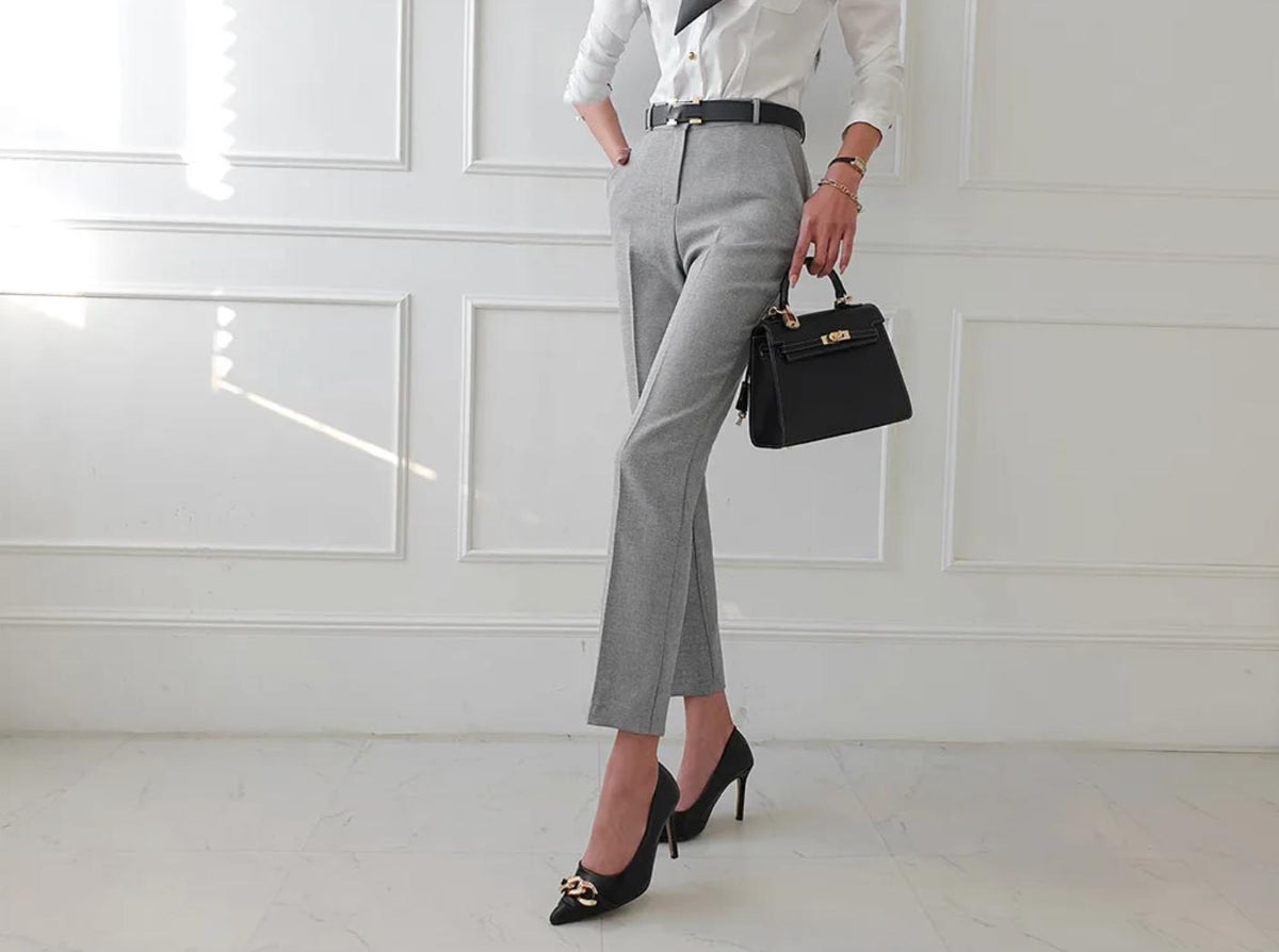 Tailored grey trousers from the Osier 3-piece suit, styled with a white shirt, black belt, handbag, and chain-detail heels.