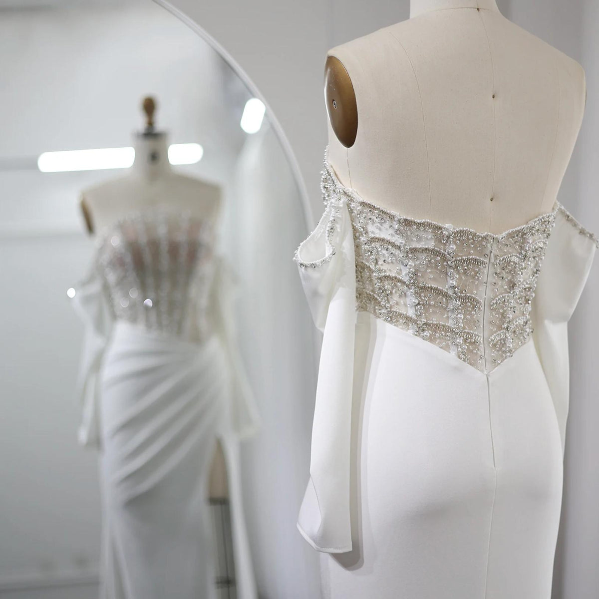 White satin mermaid gown with crystal-beaded bodice, off-the-shoulder scalloped neckline, and high slit on mannequin.