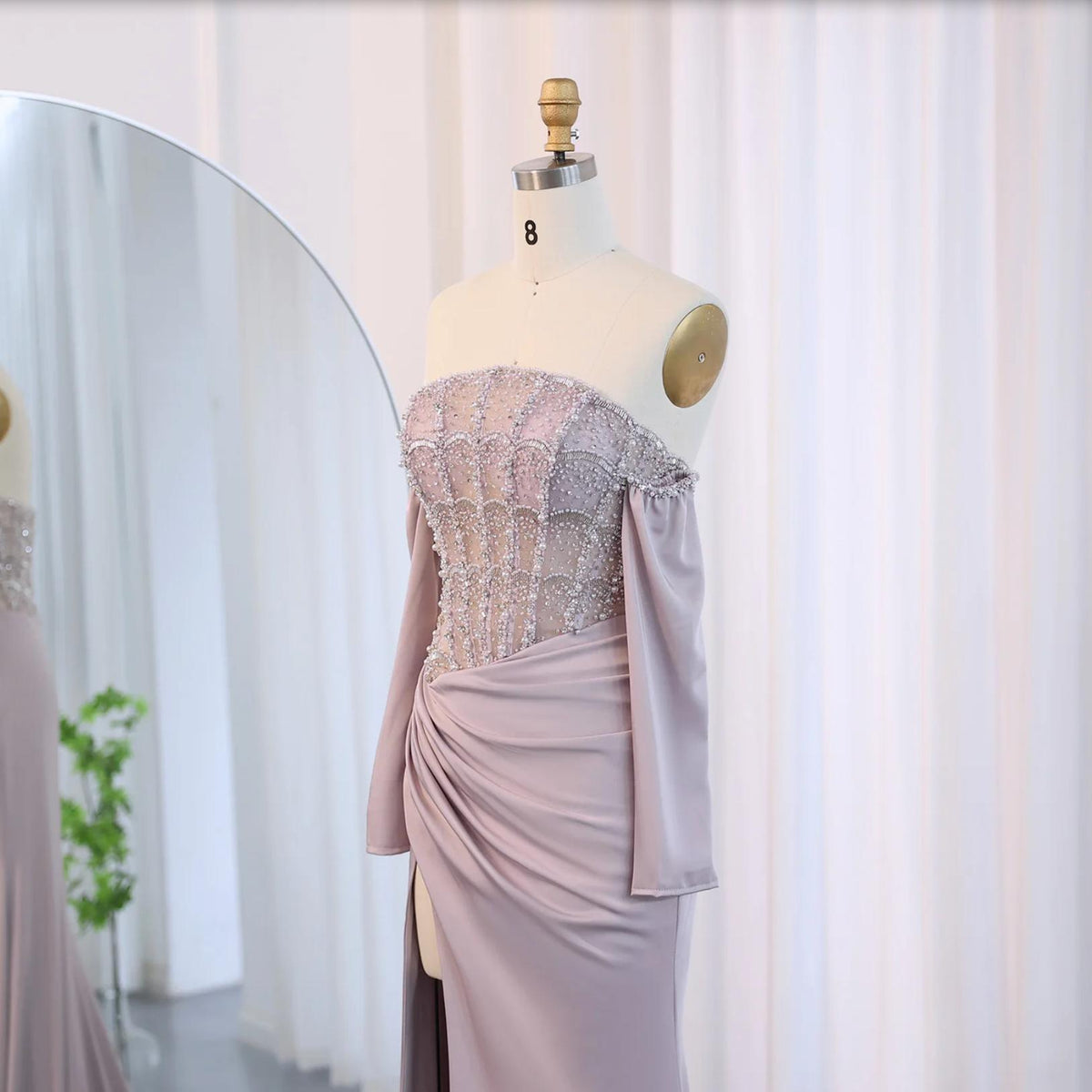 Mauve satin evening gown with a beaded corset bodice, off-the-shoulder sleeves, and a high-slit skirt on a mannequin.