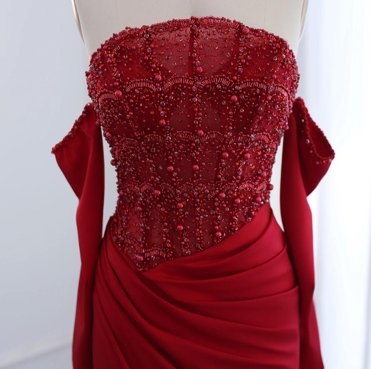 Red satin evening gown with a beaded corset bodice, off-the-shoulder scalloped neckline, and draped waist detail.
