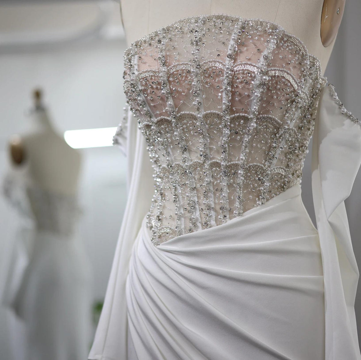 White satin evening gown featuring a beaded, crystal-embellished corset bodice and off-the-shoulder scalloped neckline.