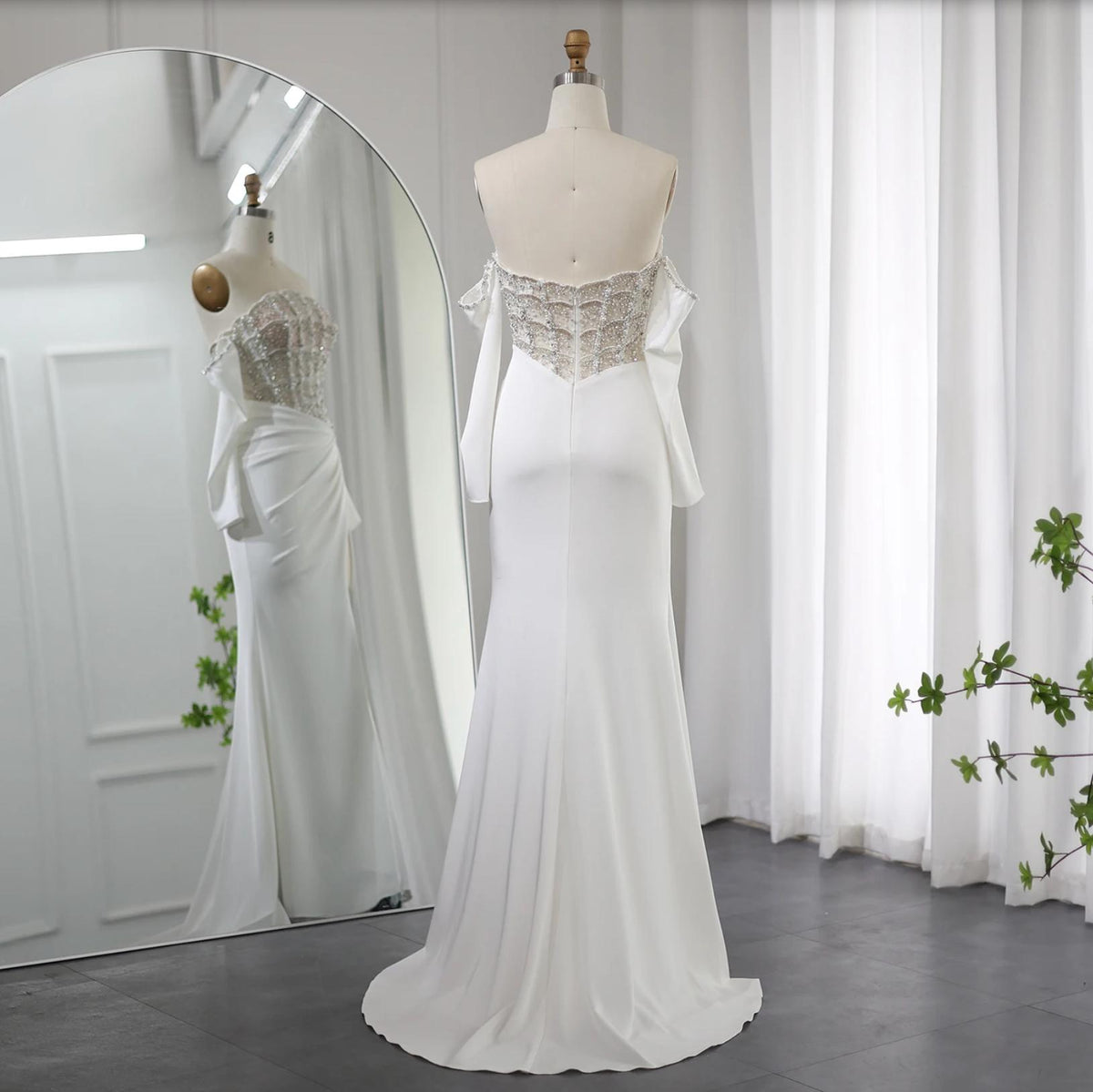 White satin mermaid evening gown with an off-the-shoulder beaded bodice and sweep train on a mannequin.