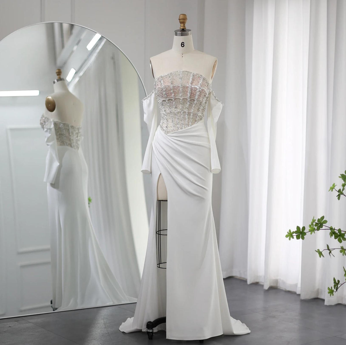 White satin evening gown with a beaded crystal bodice, off-the-shoulder neckline, and a high-slit A-line skirt.