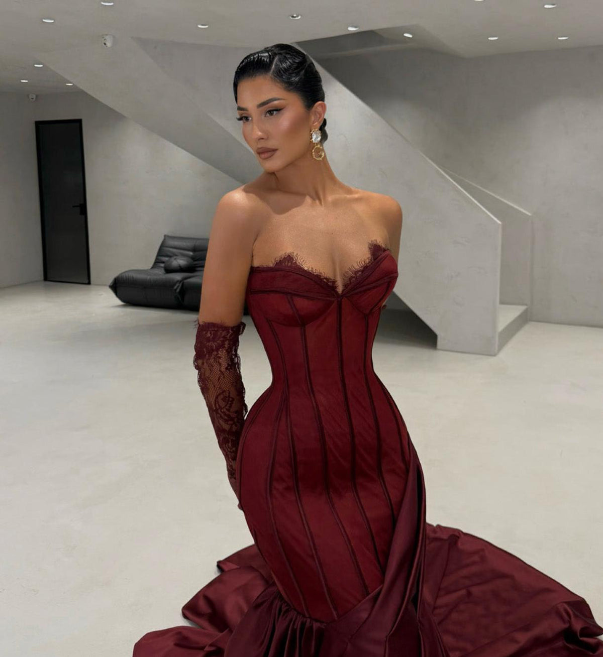 Burgundy satin corset gown with sweetheart neckline, lace detailing, and matching gloves in a modern interior.