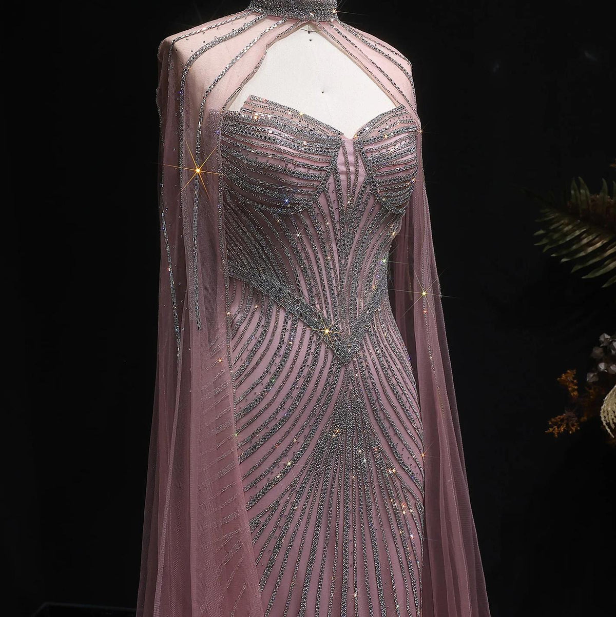 Dusty blue mermaid gown with crystal beading, sheer tulle cape sleeves, and a high-neck bodice on a mannequin.