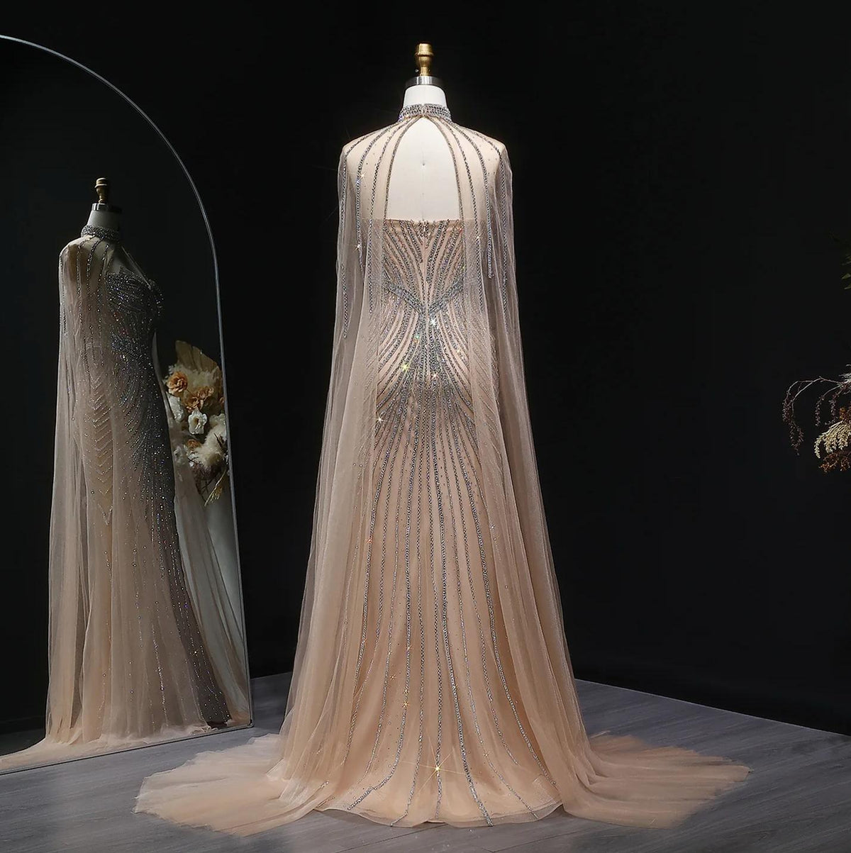 Beige tulle mermaid gown with crystal-beaded vertical patterns, dramatic cape sleeves, and a sweeping train on a mannequin.