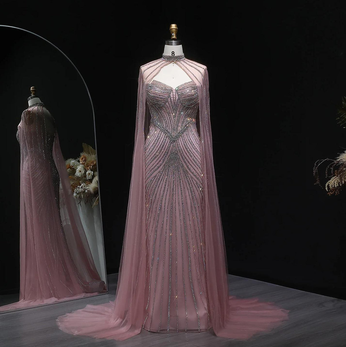 Dusty pink mermaid gown in tulle with intricate crystal beading, dramatic cape sleeves, and a sweeping train.