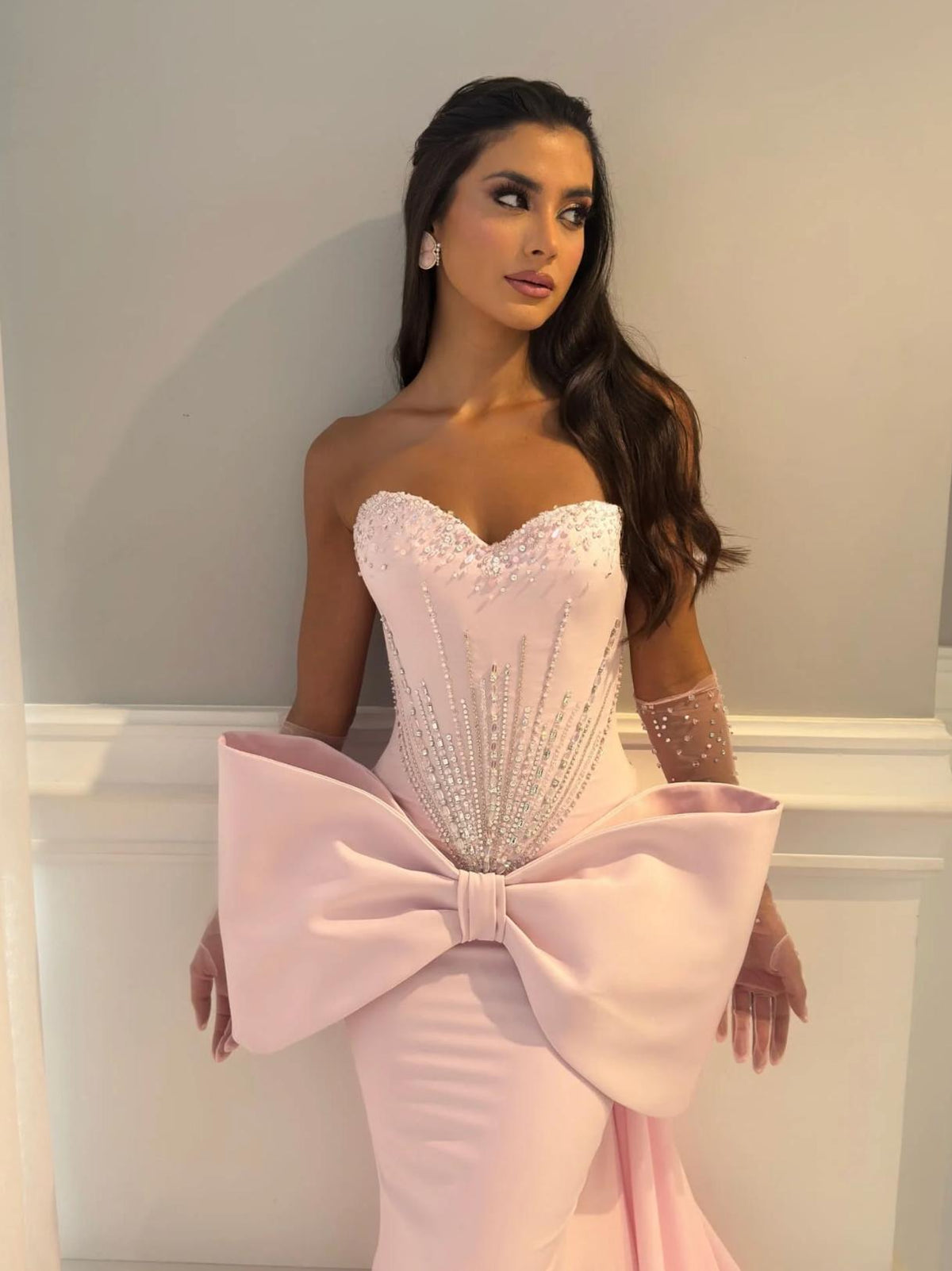 Strapless pink mermaid gown with a beaded corset bodice and a dramatic oversized 3D bow at the waist.