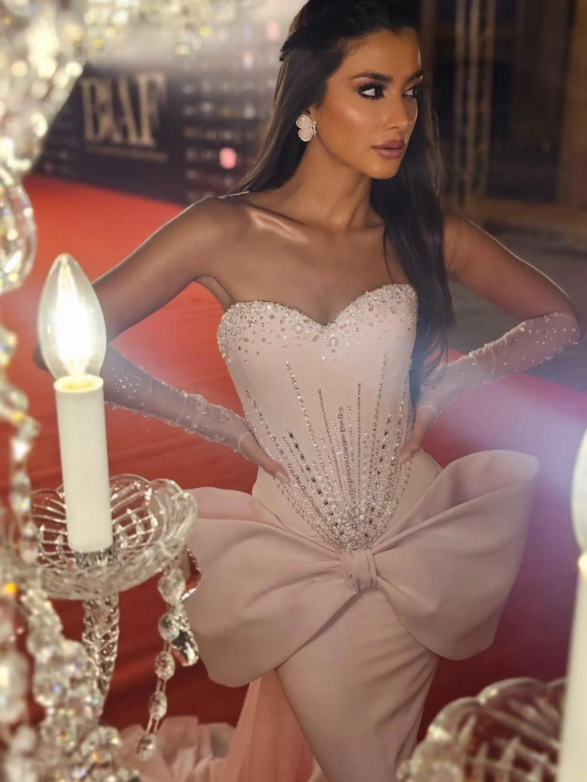 Pink strapless mermaid gown with a beaded corset bodice, sheer embellished gloves, and a dramatic 3D bow at the waist.