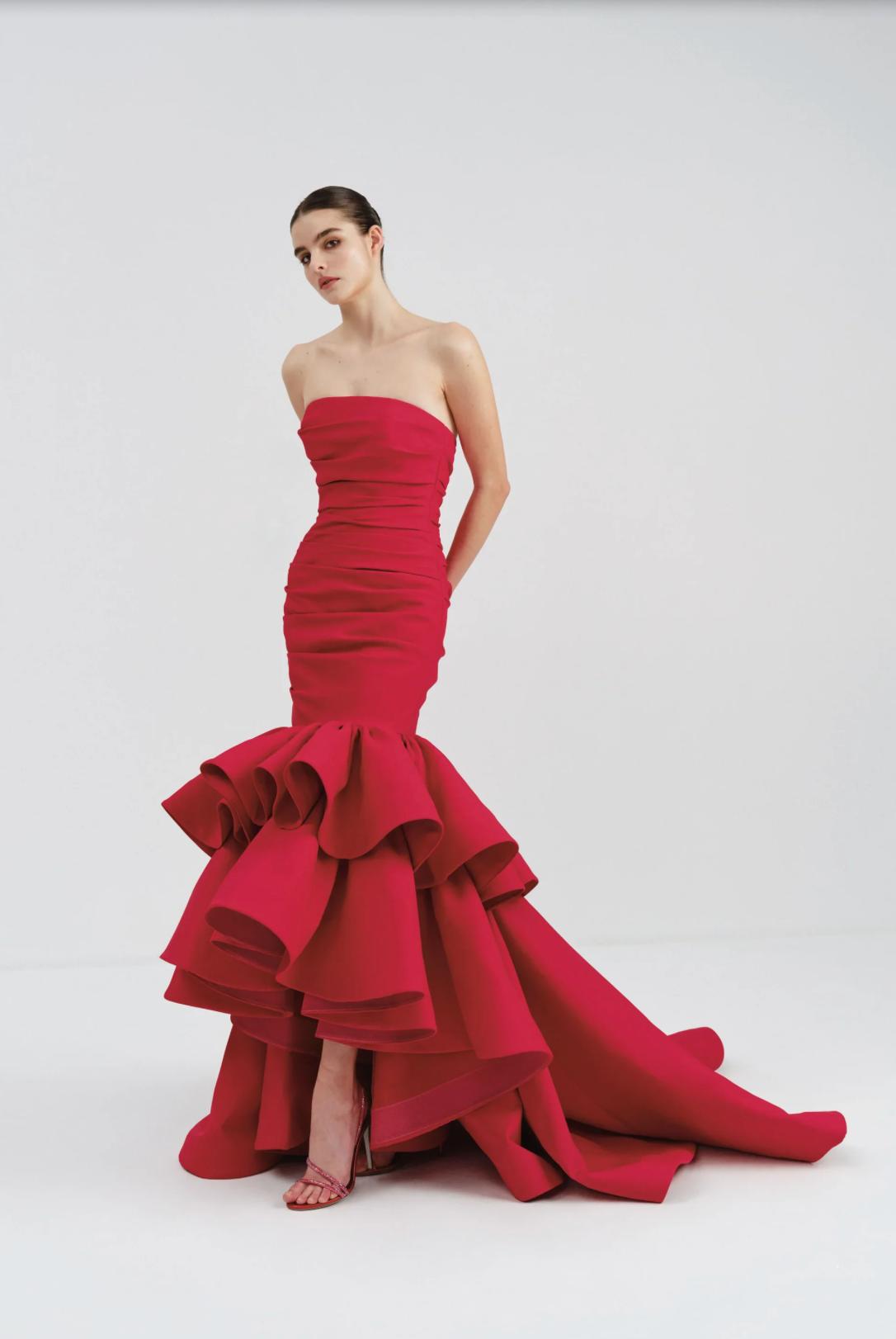 Red strapless mermaid gown in double-sided satin with a dramatic ruffled high-low hem and floor-length train.