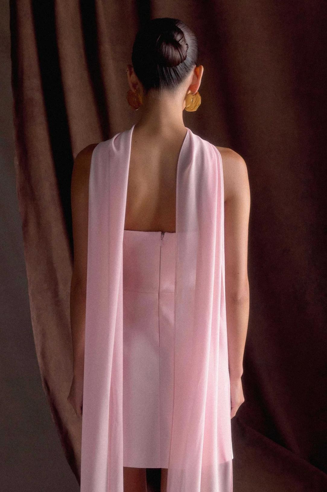 Back view of a light pink satin mini dress with a removable flowing shawl, featuring a sleek, sleeveless A-line silhouette.