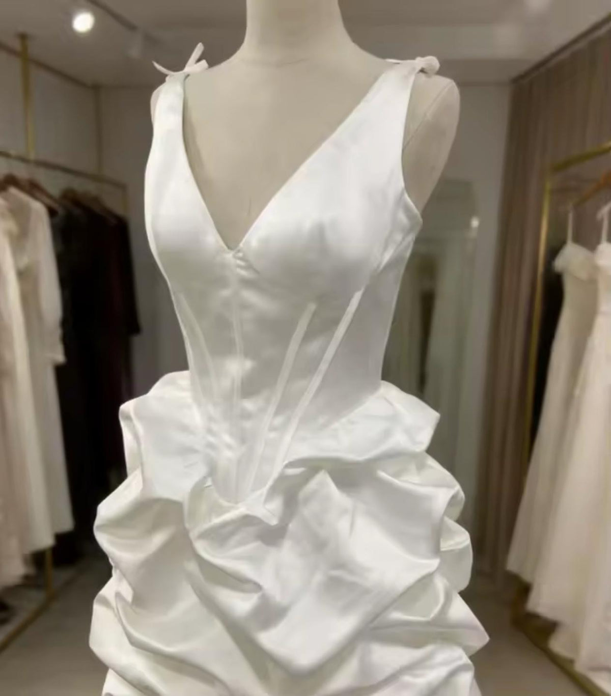 White satin mini dress with a plunging V-neck, structured corset bodice, and dramatic pleated A-line skirt on a mannequin.