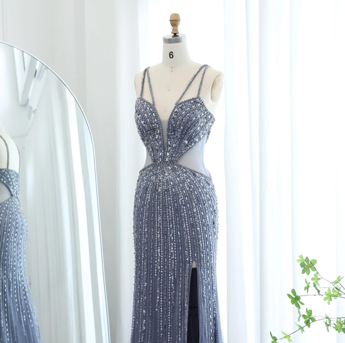 Nude mermaid evening gown with intricate beading, sequins, V-neckline, spaghetti straps, and a high leg slit on a mannequin.