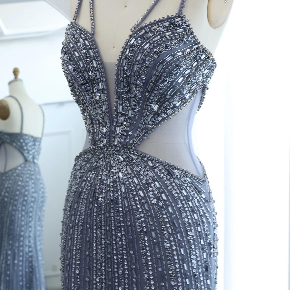 Nude mermaid evening gown with intricate crystal and sequin beading, V-neckline, and sheer tulle panels on a mannequin.