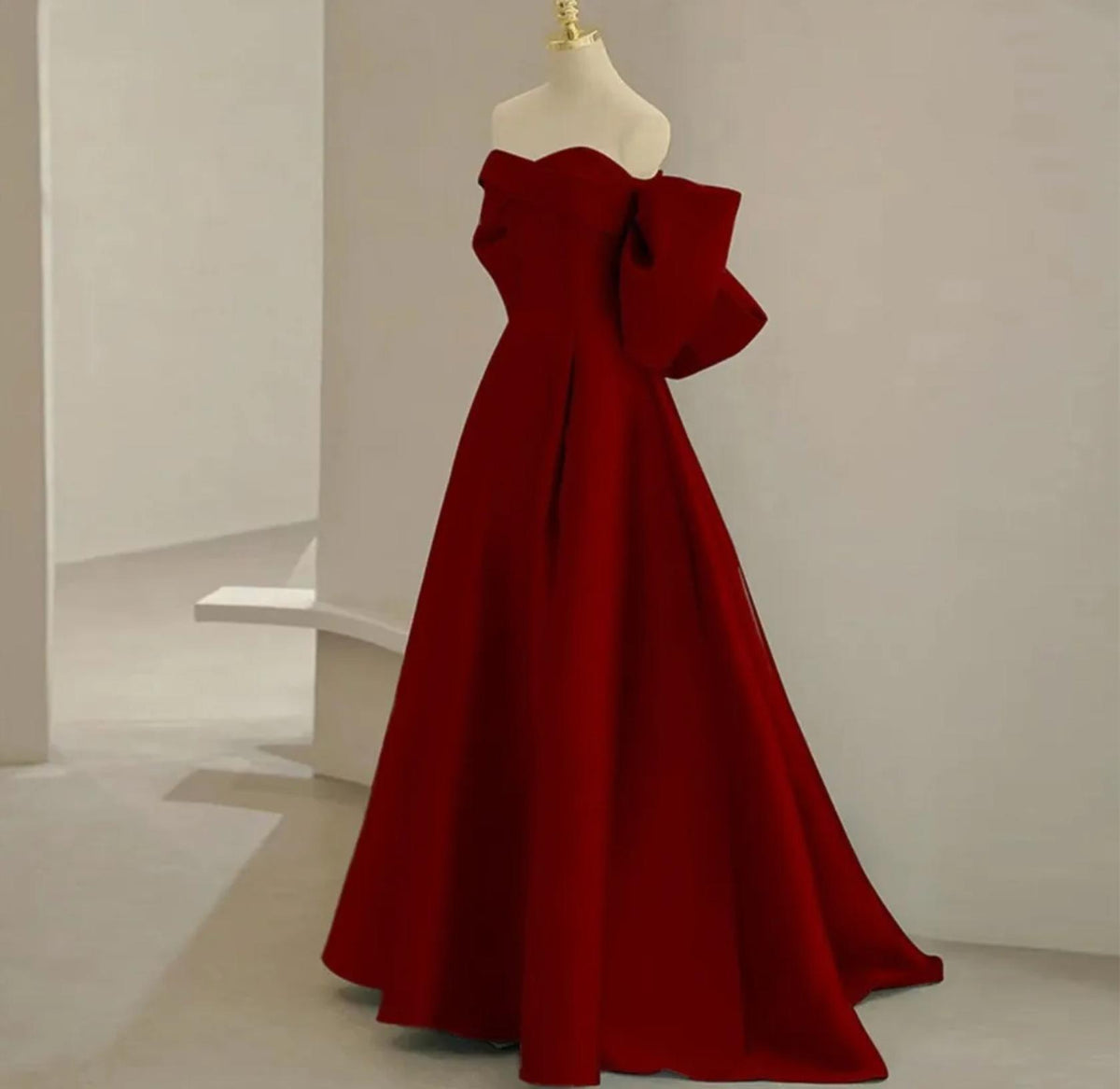 Regina Gown in deep red satin with a strapless off-the-shoulder neckline and dramatic bow detail on an A-line skirt.