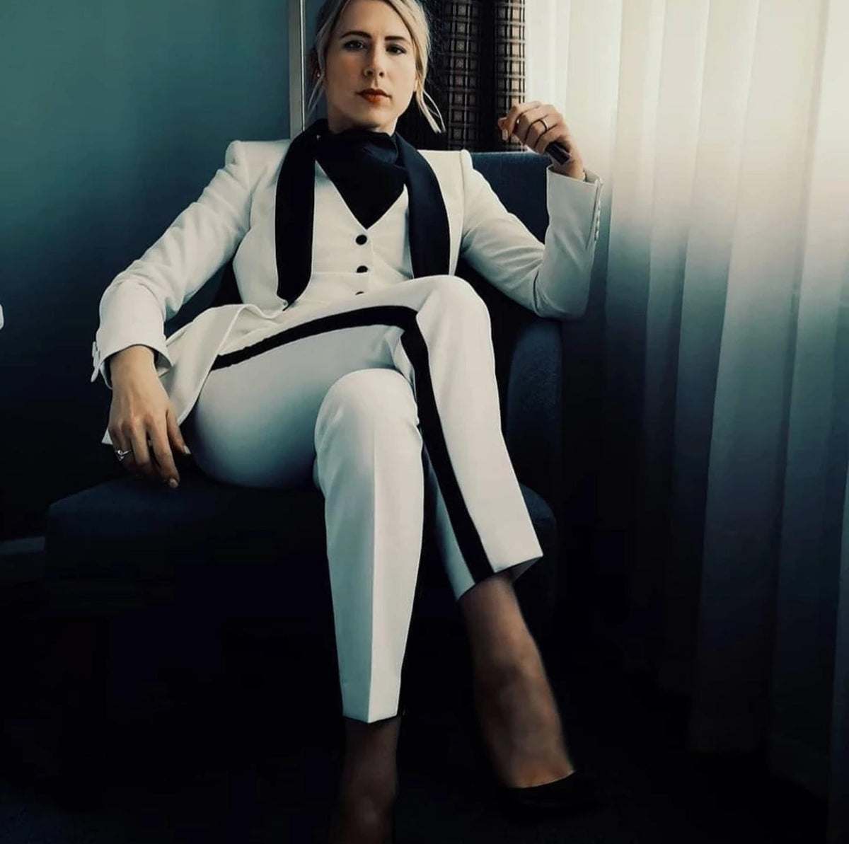 Woman wearing a tailored white three-piece tuxedo with black peaked lapels and side-stripe trousers.