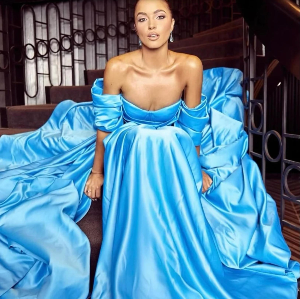 Bright blue satin A-line gown with a sweetheart neckline and off-the-shoulder sleeves, worn by a woman on a staircase.