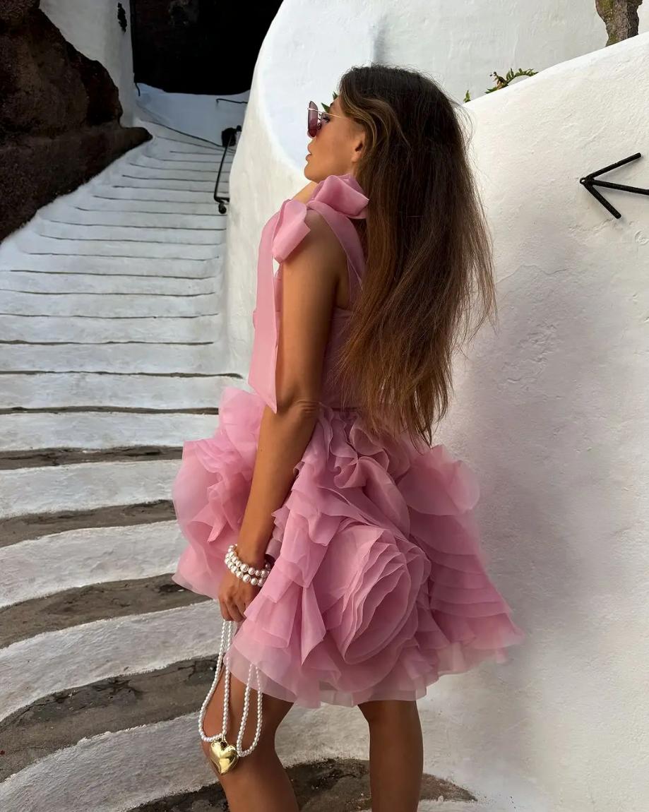 Pink organza mini dress with 3D floral details, tie straps, and a ruched silhouette on a woman standing on stairs.