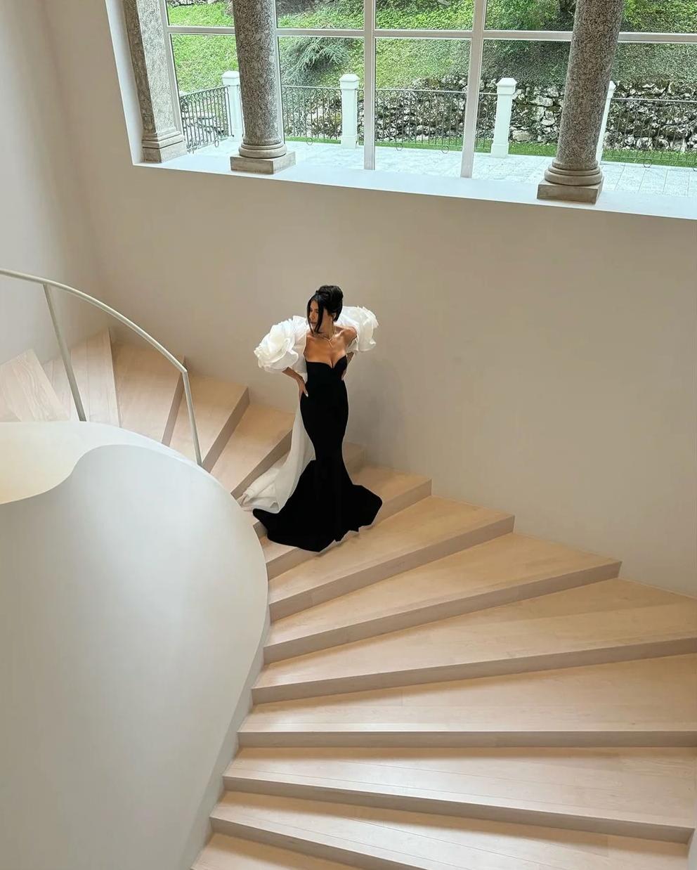 Black crepe evening gown with off-shoulder white organza ruffles and a dramatic floor-length cape train on a staircase.