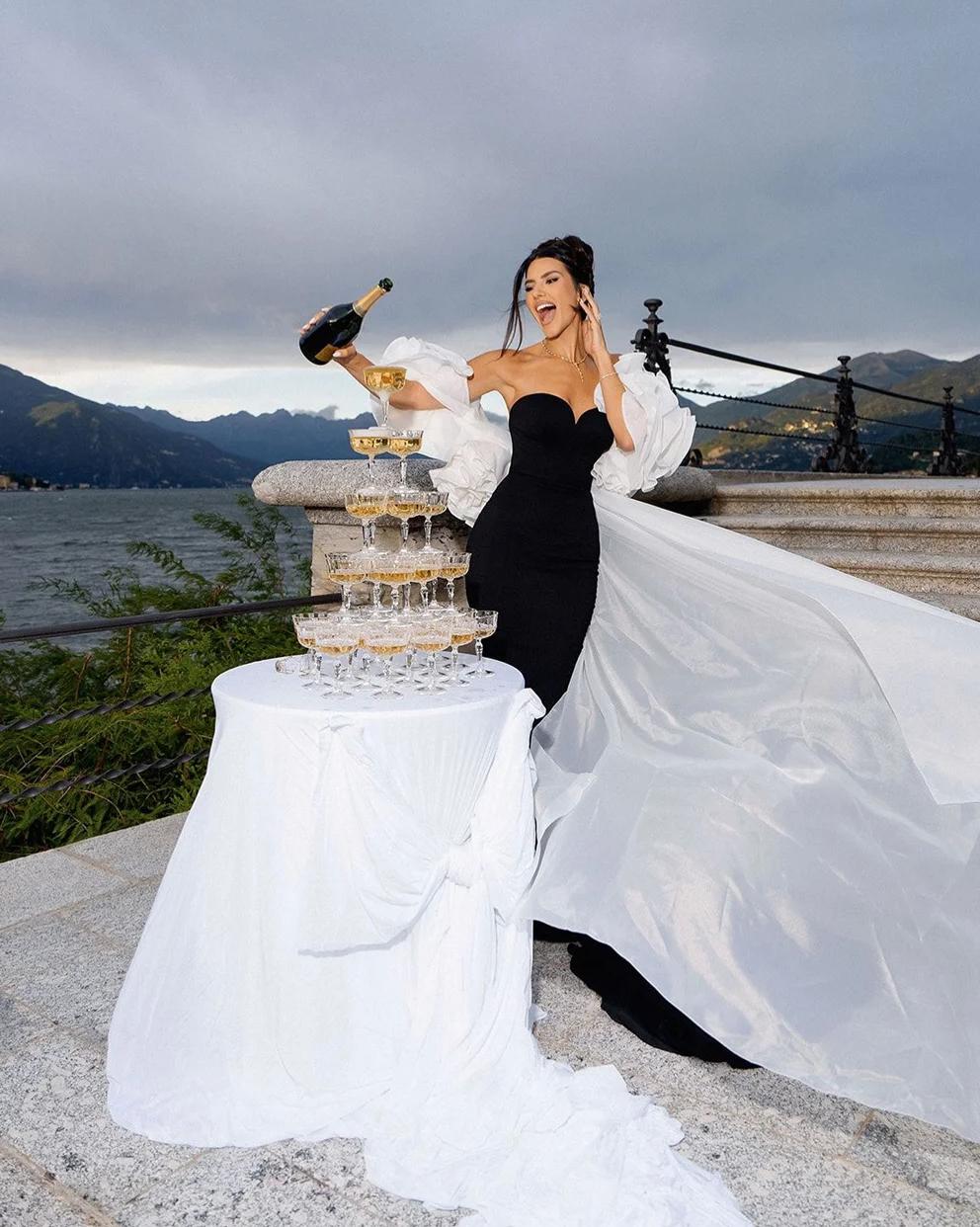 Black crepe evening gown with off-shoulder sweetheart neckline, white organza ruffles, and a dramatic long cape train.