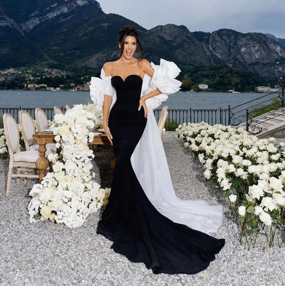 Black crepe evening gown with off-shoulder sweetheart neckline, white organza ruffles, and a dramatic floor-length cape train.