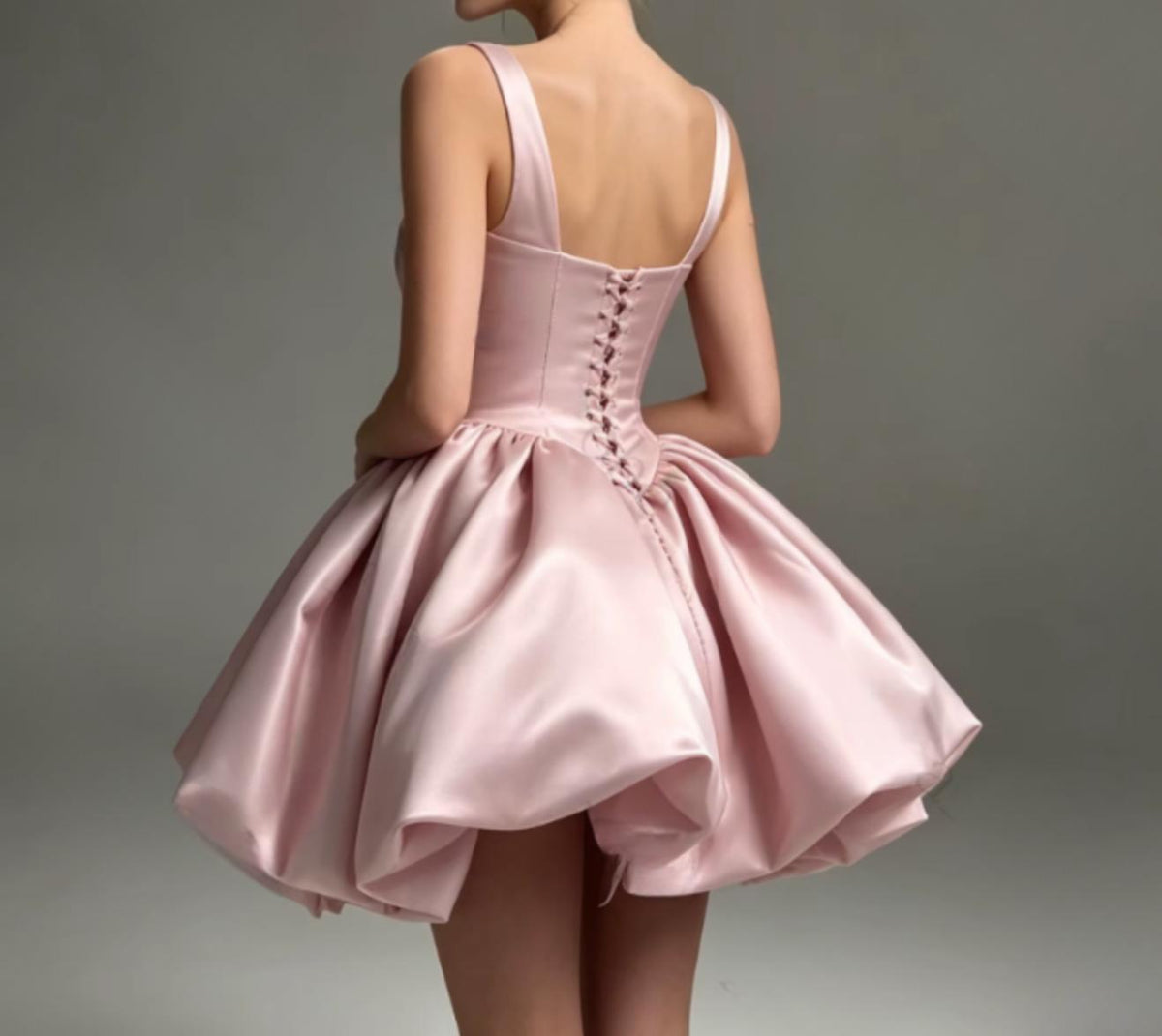 Pink satin mini dress with a corset-inspired lace-up back and a voluminous, sculptural bubble skirt.