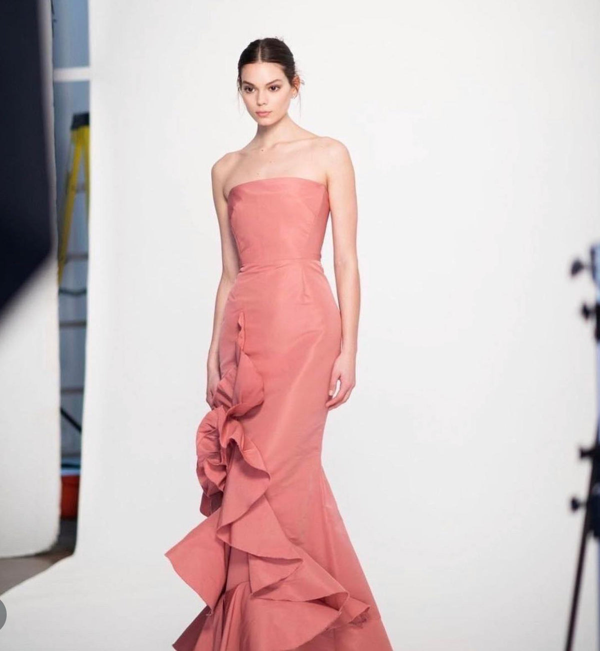 Strapless coral faille gown with a fitted bodice and cascading ruffled side detail on a white studio background.