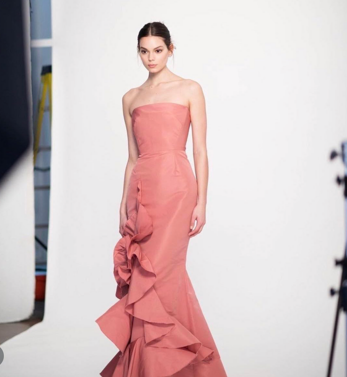 Strapless coral faille gown with a fitted bodice and cascading ruffled side detail on a white studio background.