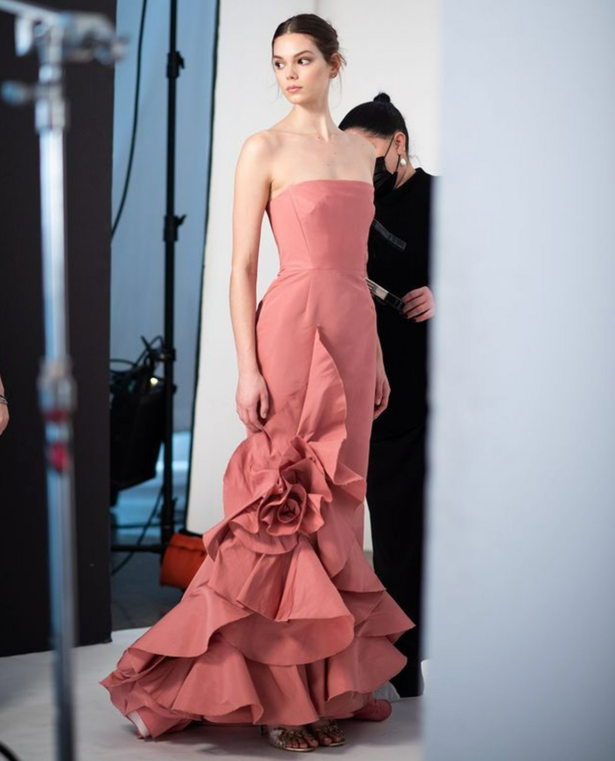 Model wearing a fitted, dusty rose faille gown with a strapless bodice and a large 3D floral ruffle detail on the skirt.