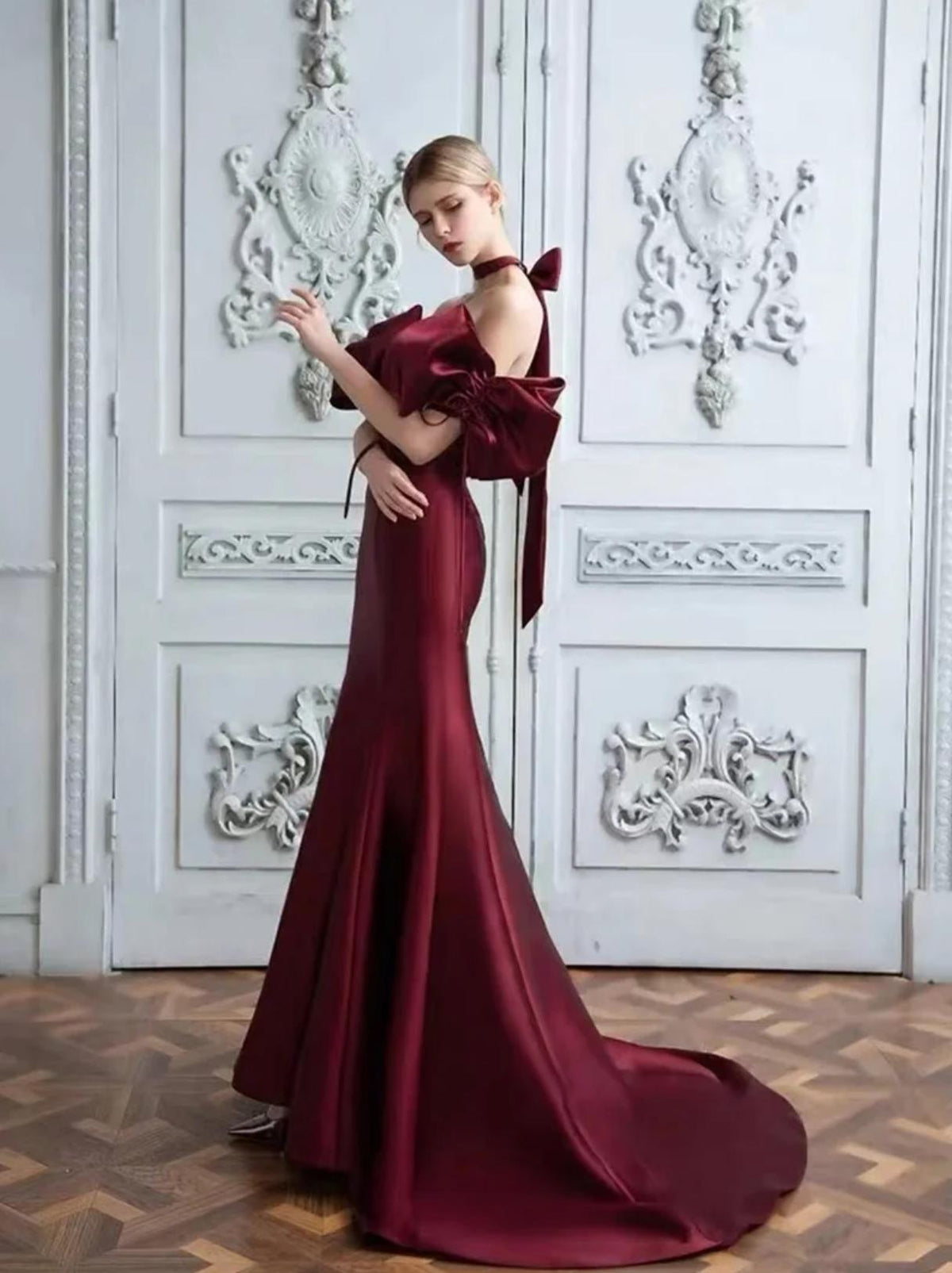 Burgundy satin mermaid gown with off-the-shoulder neckline, dramatic bow sleeves, and floor-length train.