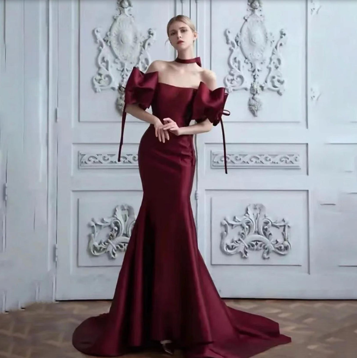 Burgundy satin mermaid gown with off-the-shoulder neckline, dramatic 3D bow sleeves, and a floor-length sweeping hem.