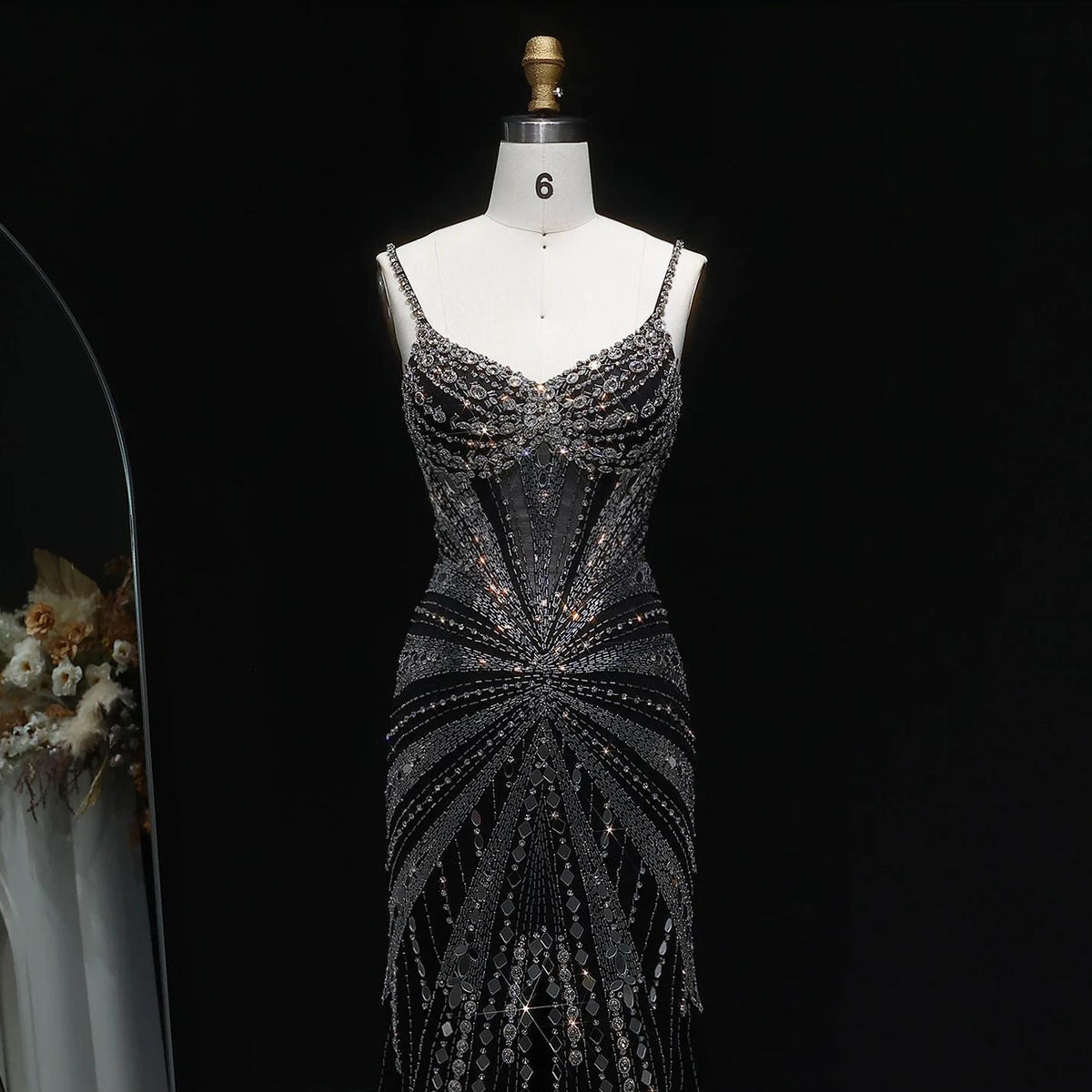 Black satin evening gown with intricate crystal beading, spaghetti straps, and a form-fitting silhouette on a mannequin.
