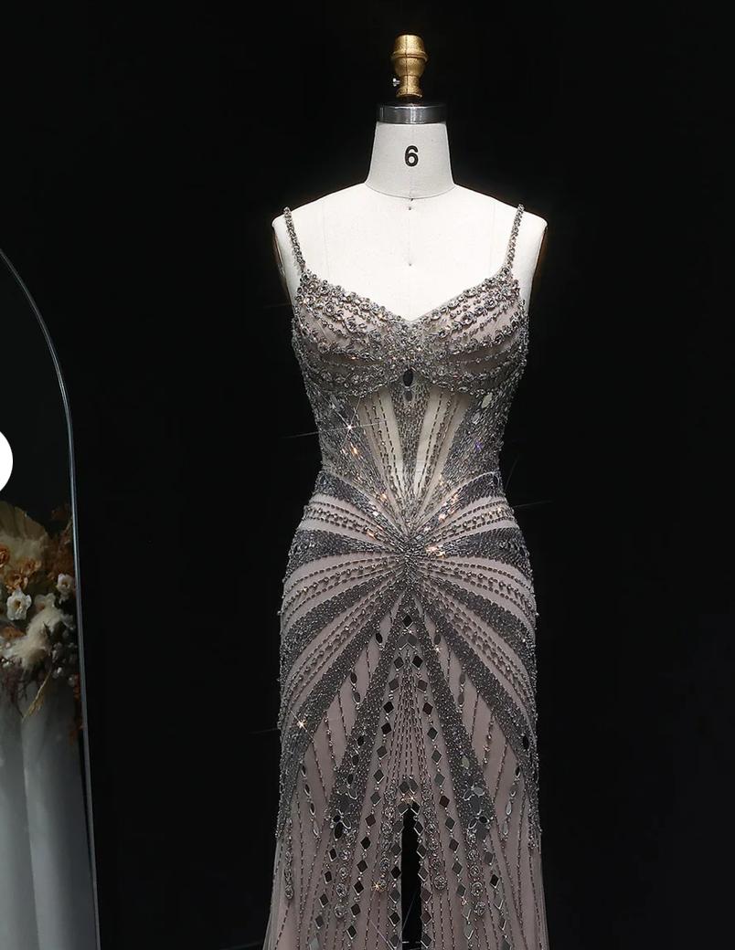 Champagne satin gown with intricate crystal beading, spaghetti straps, and a sheer, form-fitting silhouette on a mannequin.