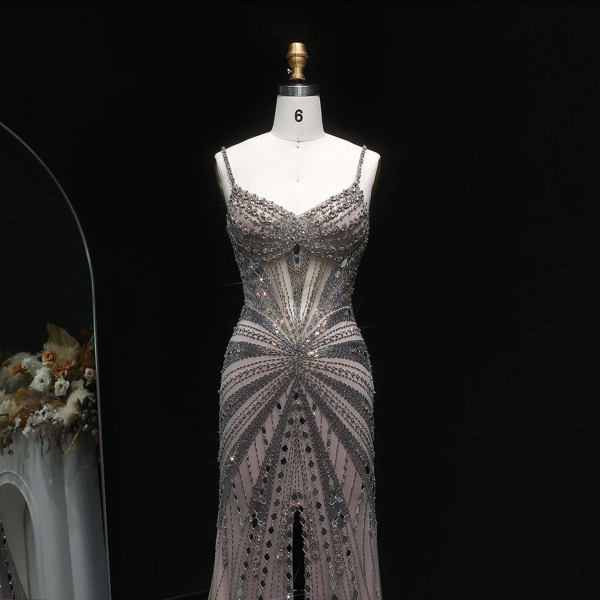 Champagne satin luxury gown with intricate crystal beading, spaghetti straps, and a sheer bodice on a mannequin.