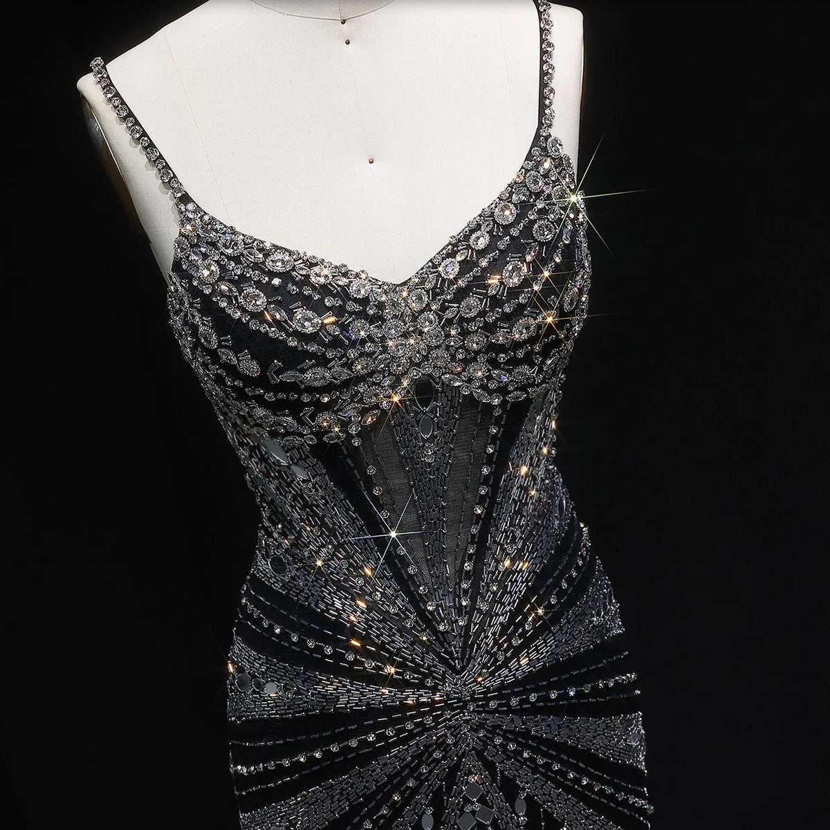 Black satin evening gown with spaghetti straps, intricate crystal beading, and a sheer bodice on a mannequin.