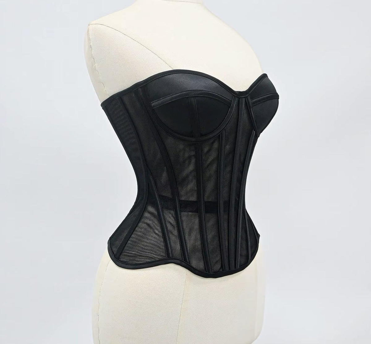 Black waist-cinching corset with sculpted cups, steel boning, and sheer mesh tubing on a mannequin.