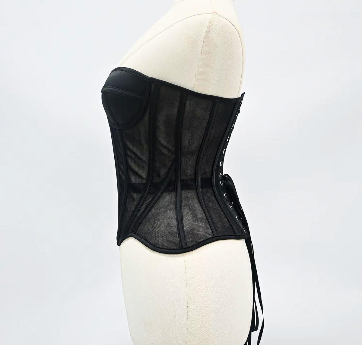 Black steel-boned corset with mesh tubing, structured cups, and lace-up back detailing on a mannequin.