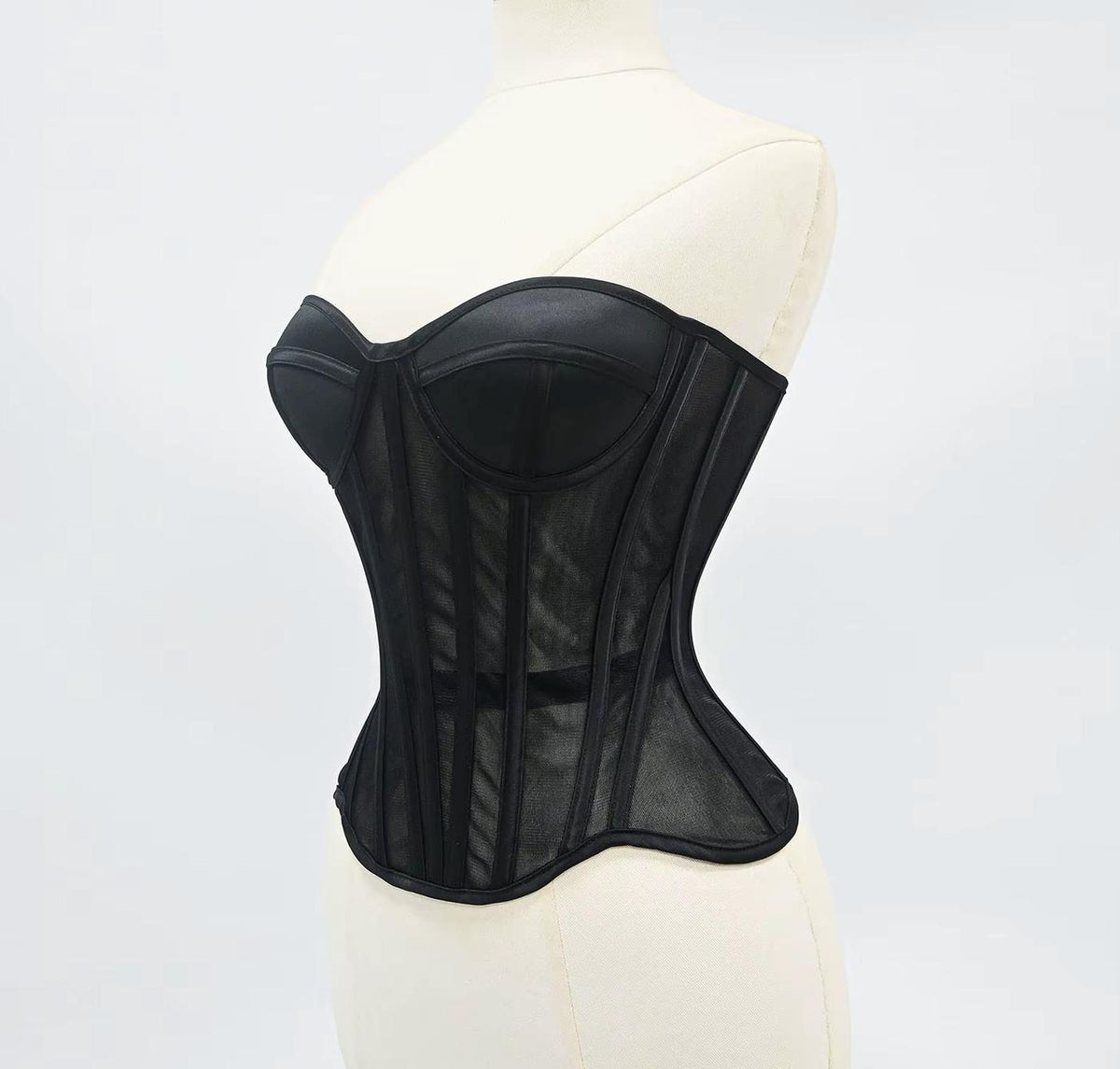 Black waist-cinching corset with sculpted cups, steel boning, and sheer mesh panels on a mannequin.