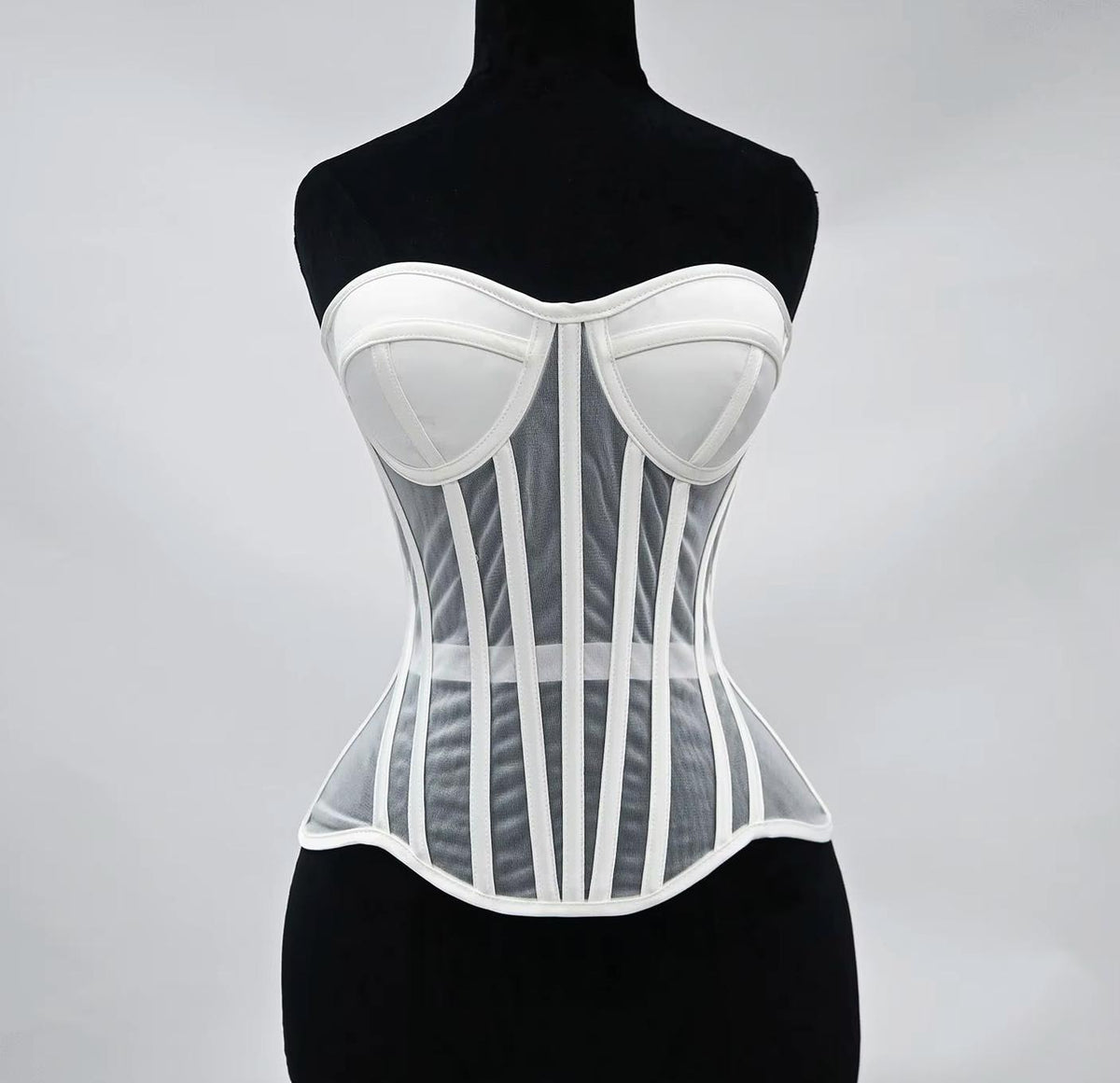 White waist-cinching corset with structured cups, steel boning, and sheer mesh panels on a black mannequin.