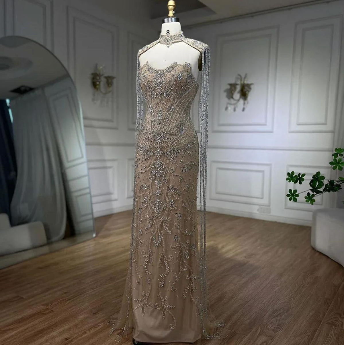 Beaded mermaid gown with shimmering crystals, sequins, and long tassels on a mannequin in a bright studio.