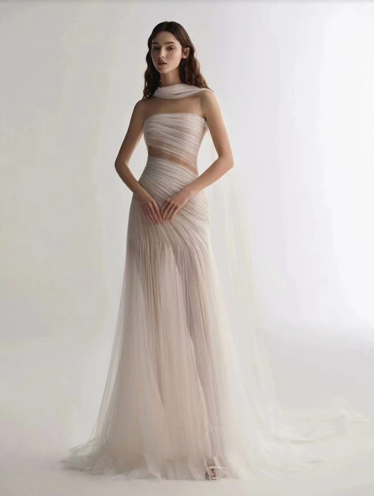 A woman wearing the Old Money Collection La Digue Gown with a sheer neck and pleated tulle, featuring a long ribbon.