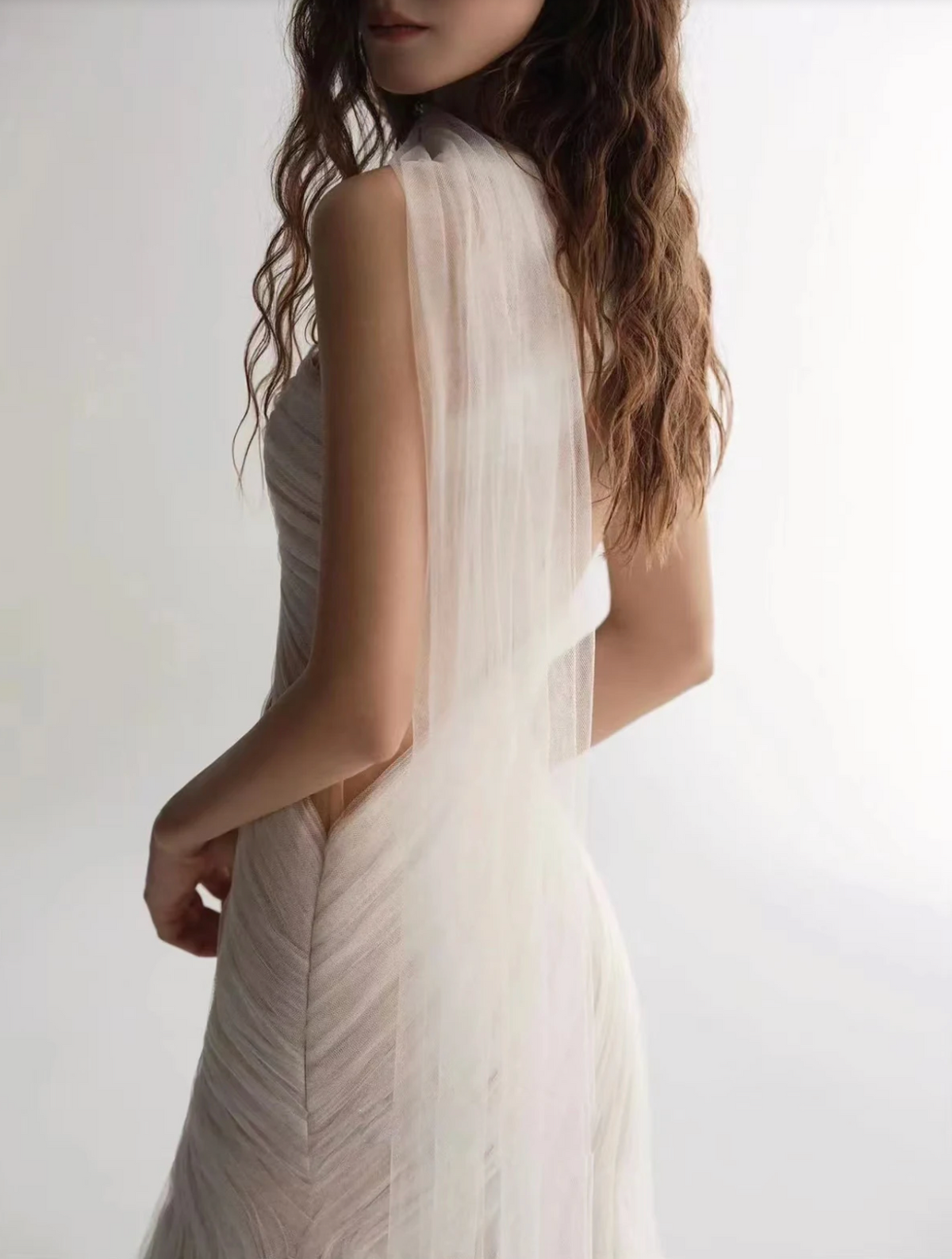 A woman wearing the Old Money Collection La Digue Gown with a sheer neck and pleated tulle, featuring a long ribbon.