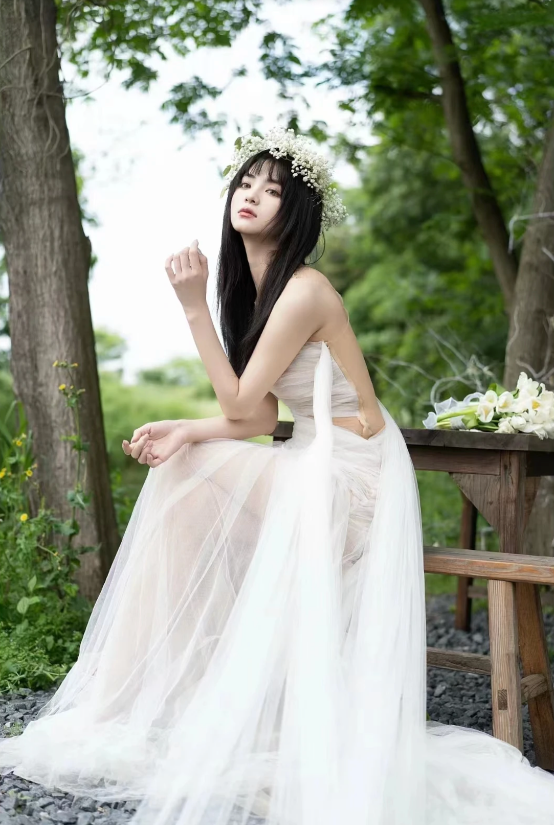 A woman wearing the Old Money Collection La Digue Gown with a sheer neck and pleated tulle, featuring a long ribbon.