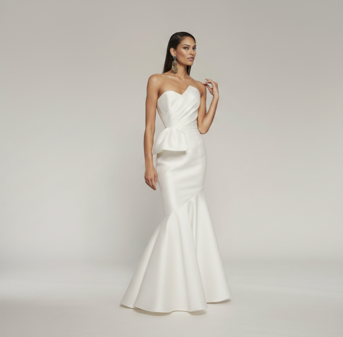 White strapless mermaid gown in pleated satin with a fitted bodice, peplum waist detail, and a dramatic flared floor-length skirt.