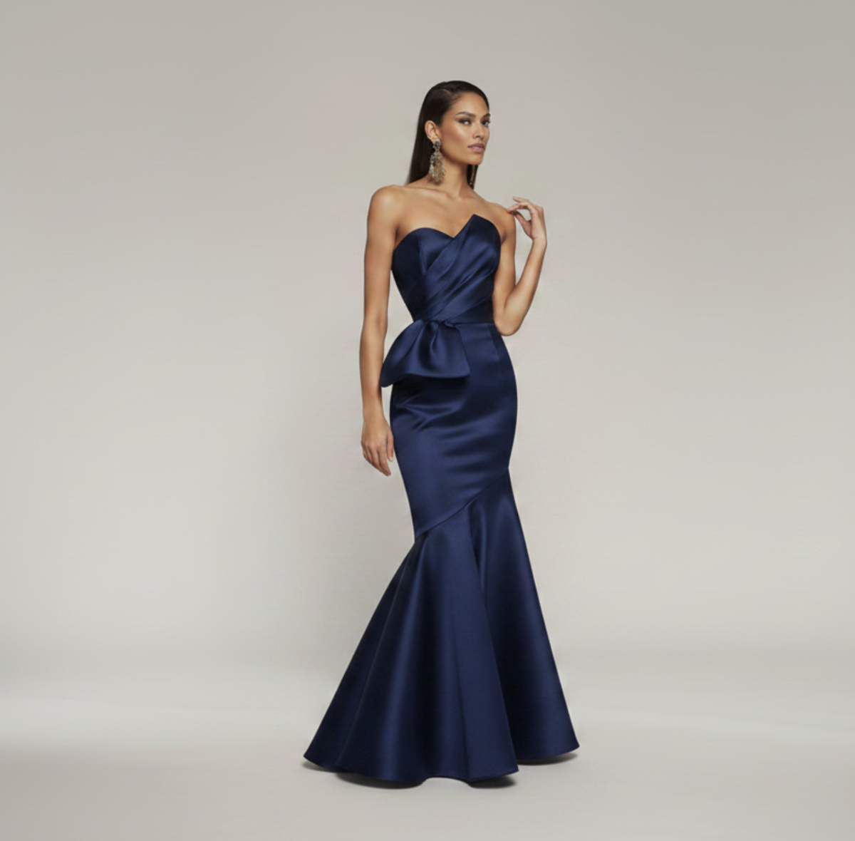 Sleeveless navy blue satin mermaid gown with a pleated bodice, peplum waist, and floor-length flared skirt.
