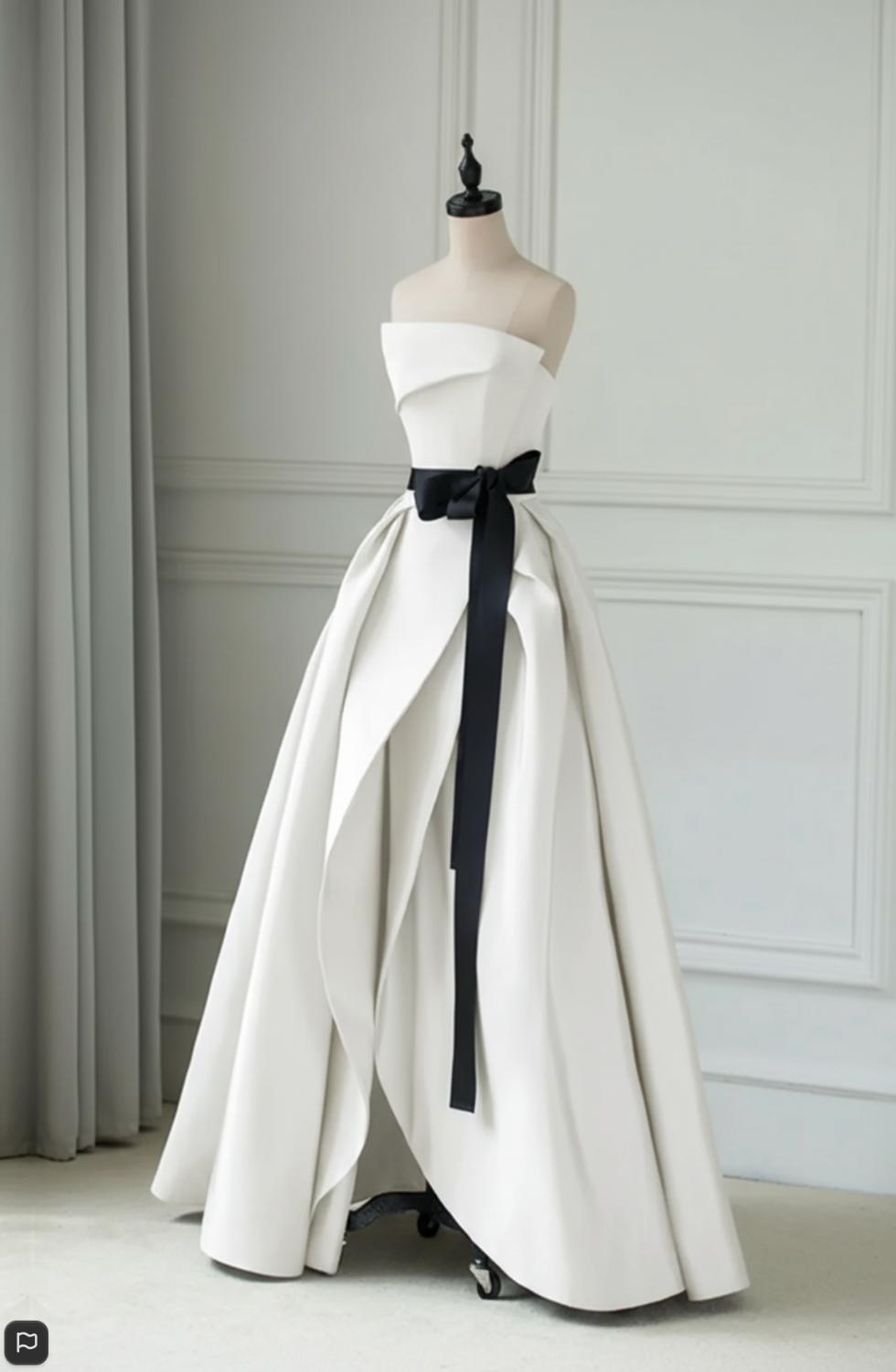 Strapless white A-line Crete gown with a dramatic black sash, pleated satin twill fabric, and floor-length silhouette.